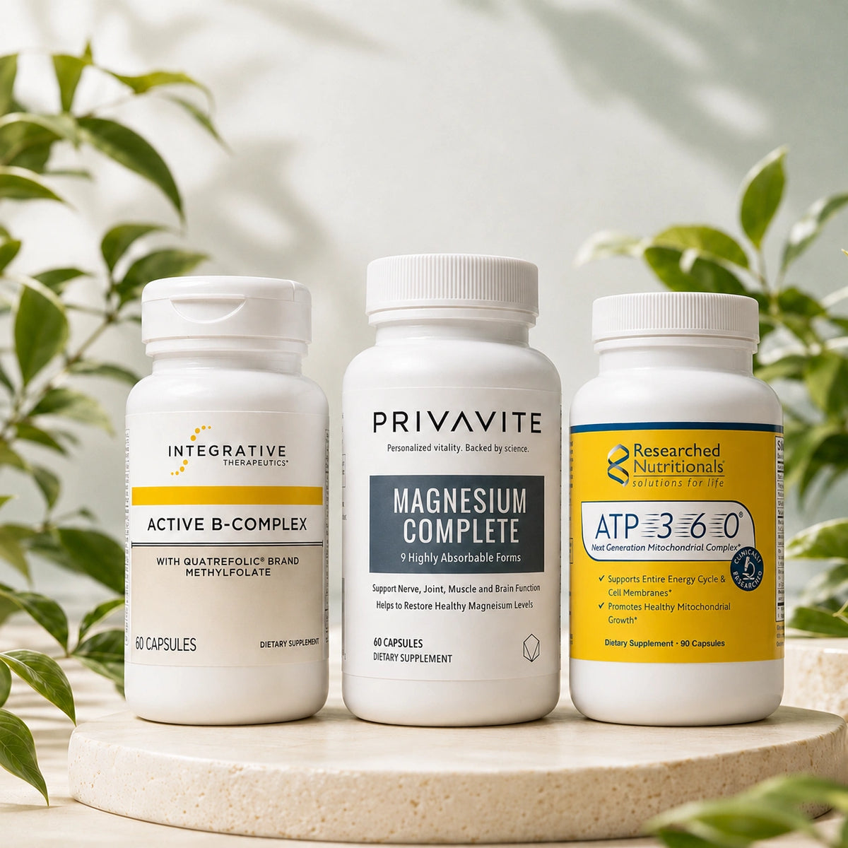 Integrative Therapeutics Active B-Complex, Privavite Magnesium Complete, and Researched Nutritionals ATP 360 supplement bottles displayed on a stone pedestal with green plants